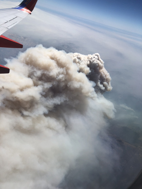 Large plume of smoke seen from an airplane, with airplane wing in view.